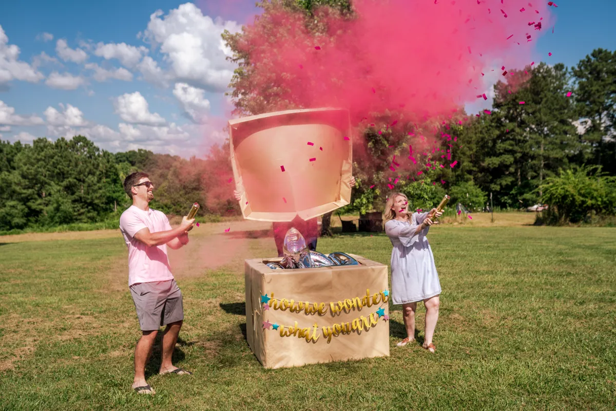 A couple setting off pink powder cannons at an outdoor gender reveal