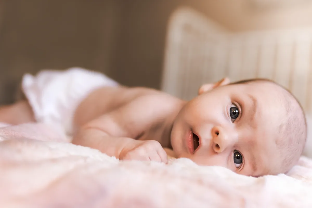 A newborn lying on a soft blanket, looking toward the camera