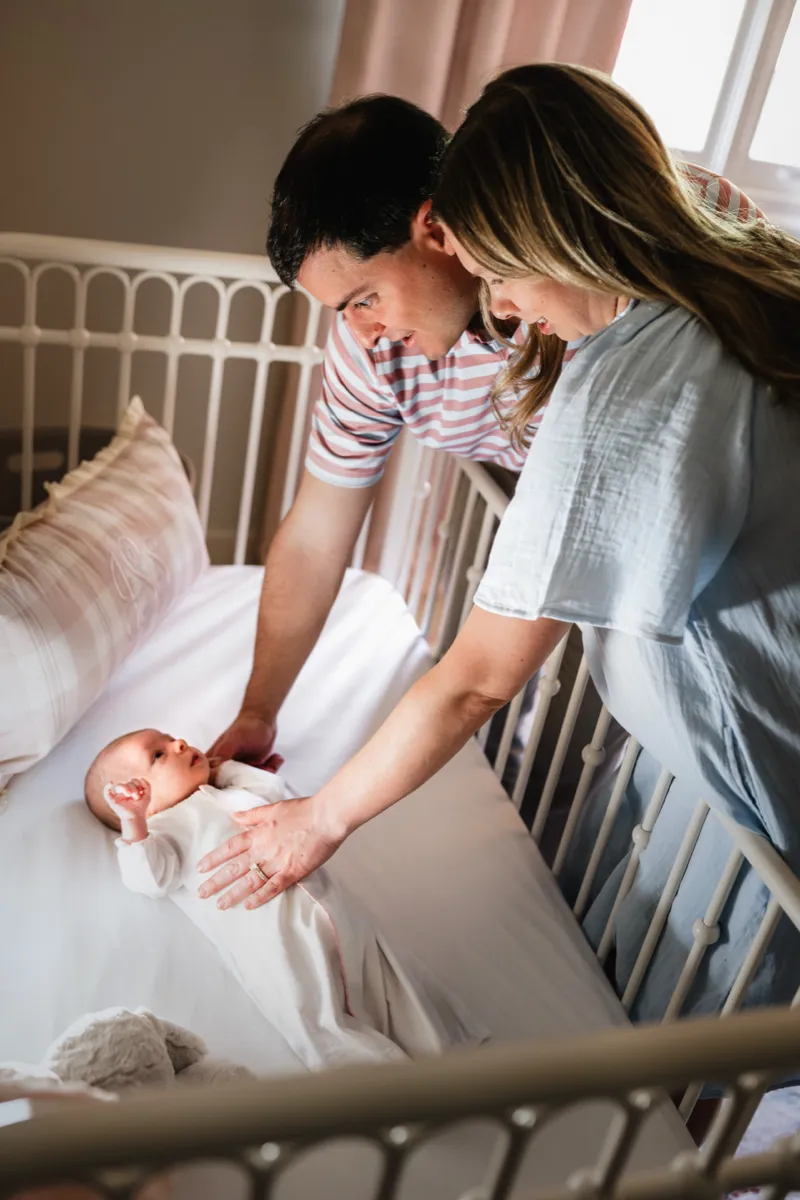 Two parents leaning over a crib to settle their newborn