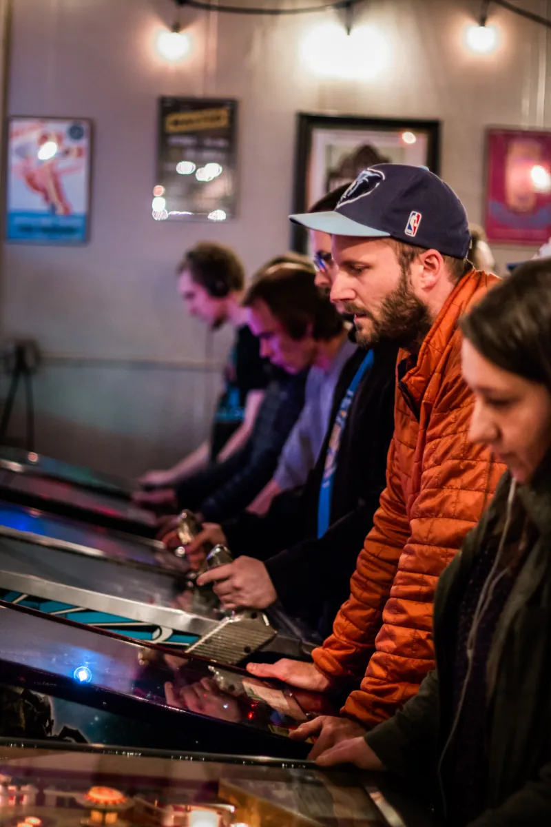 Players stand shoulder to shoulder along a row of machines under warm ceiling lights.