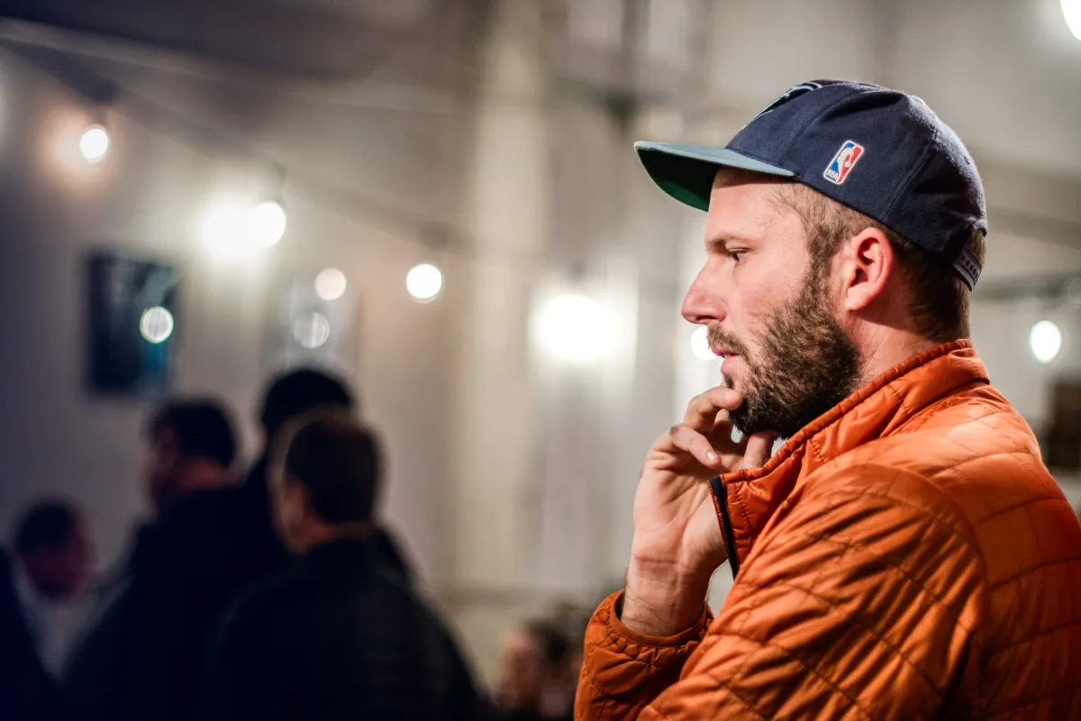A player watches the room in profile, a string of bulbs blurred behind him.