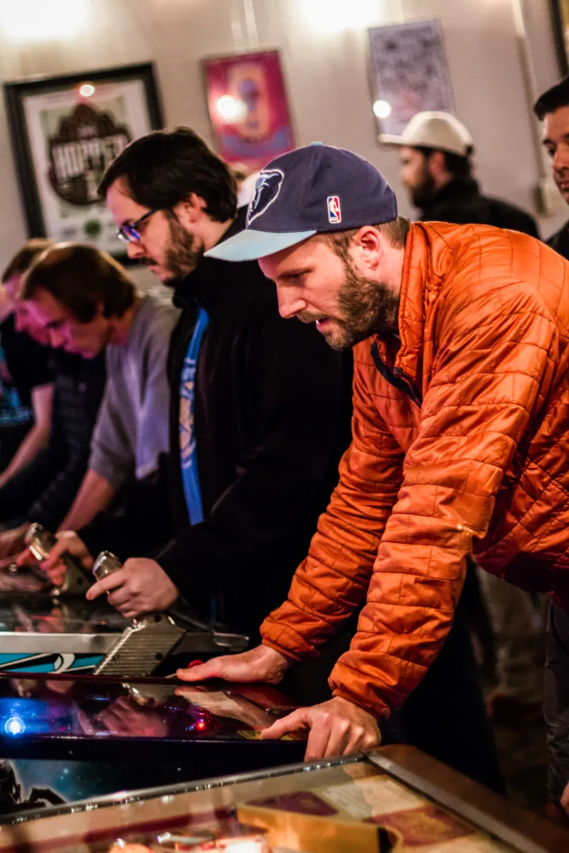 A line of players concentrates along the row, plunger handles drawn back.