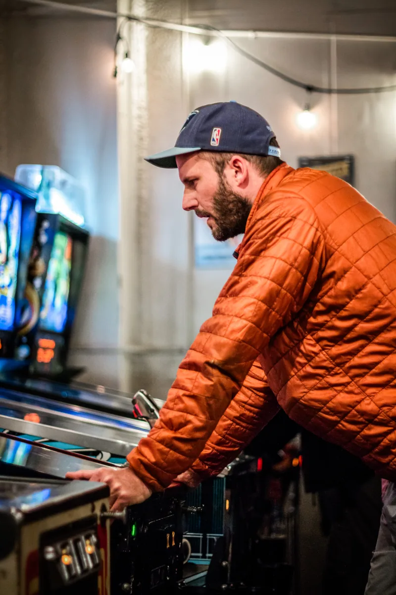 A player braces against a machine, the room's columns and hanging bulbs behind him.