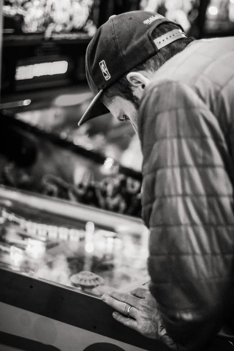 In black and white, a player bows his head over the glass, one hand resting on the cabinet.