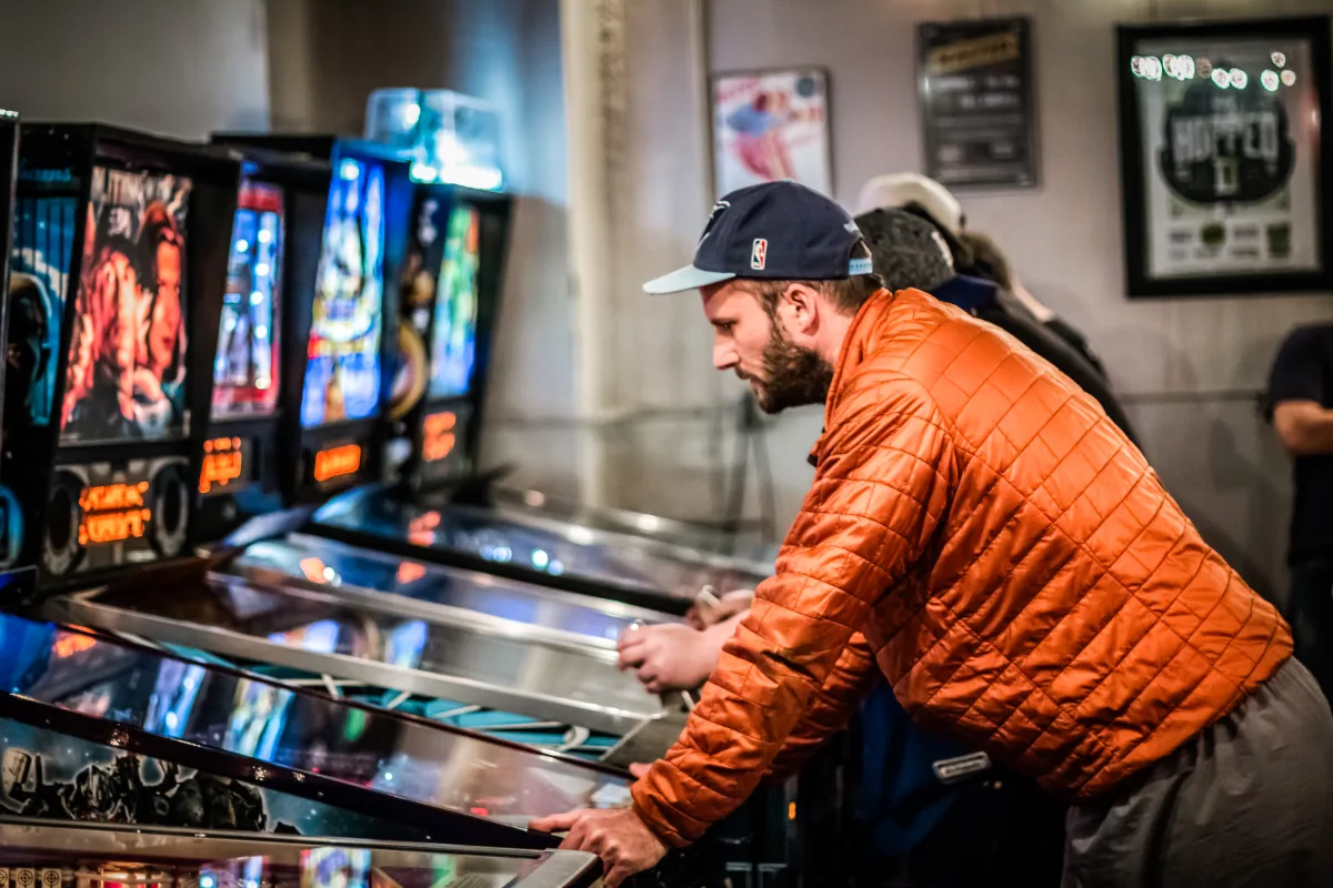 A player works the flippers at the head of the row, backglasses glowing blue.
