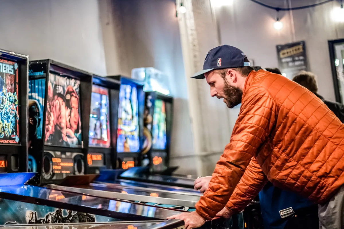 A player at the machines with the wide room and its hanging bulbs behind him.