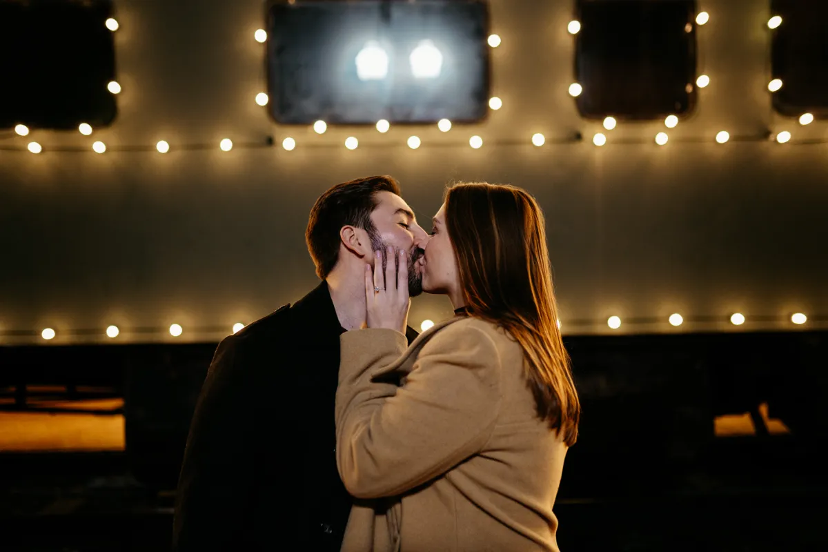 A couple kissing in front of a lit airstream trailer at night