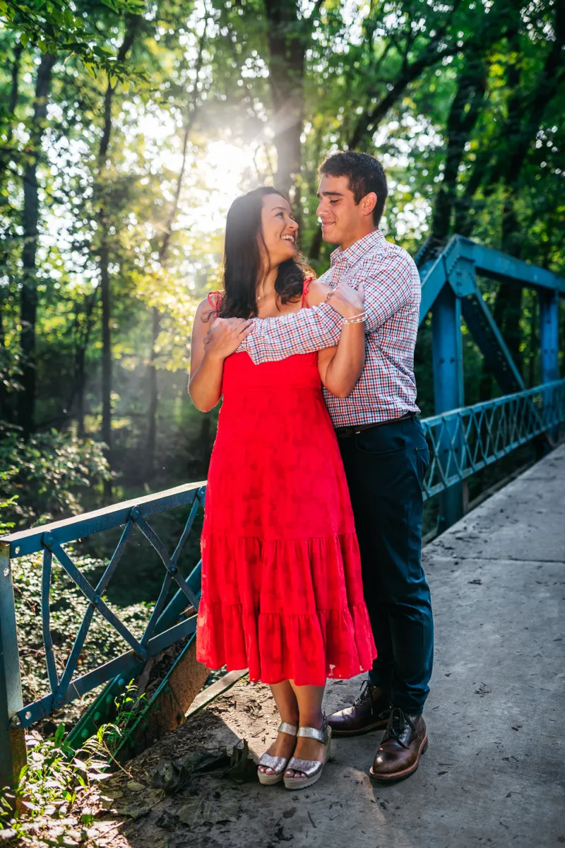 A couple in a red dress and checked shirt embracing on a green footbridge