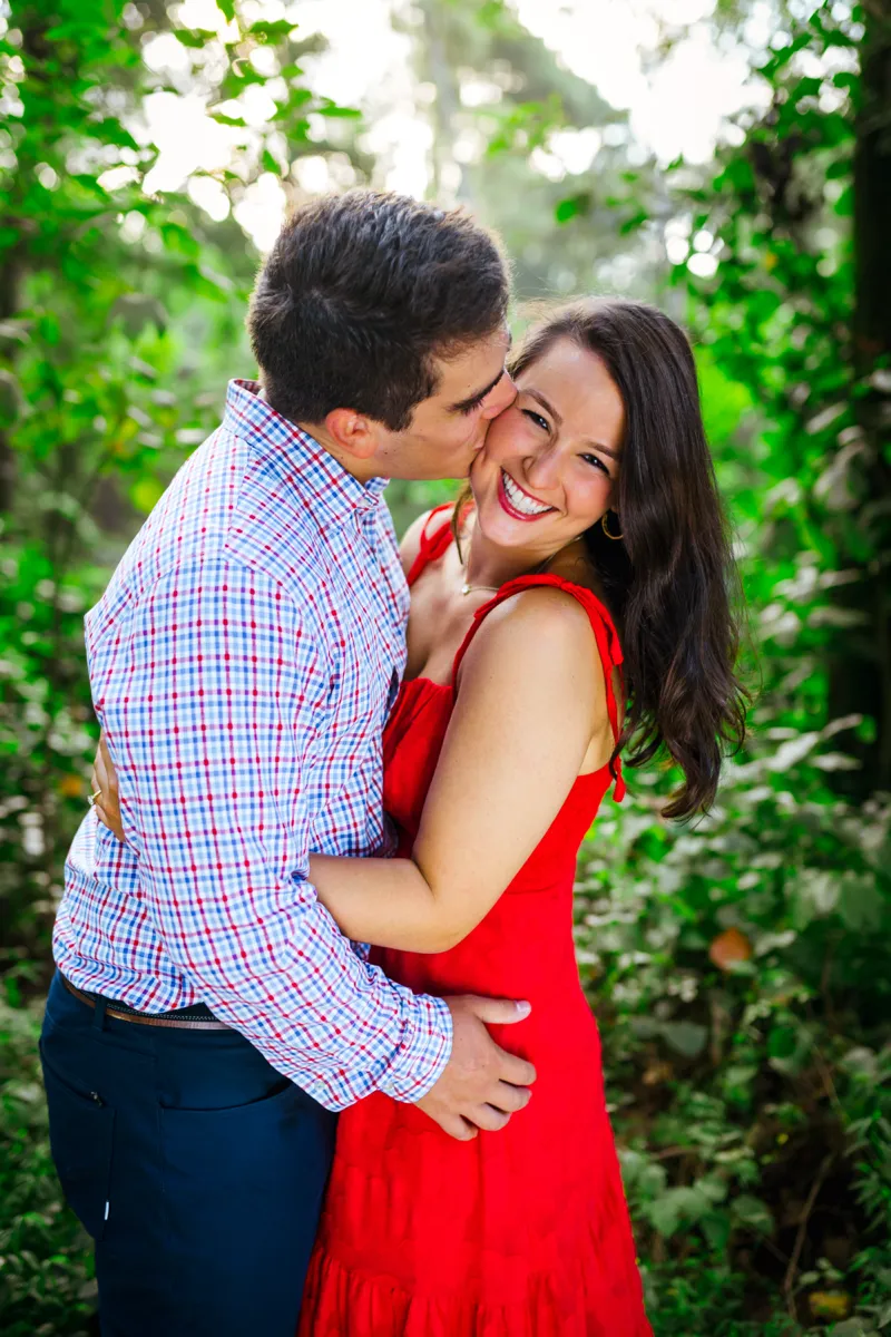 A man kissing his laughing partner on the cheek among summer greenery