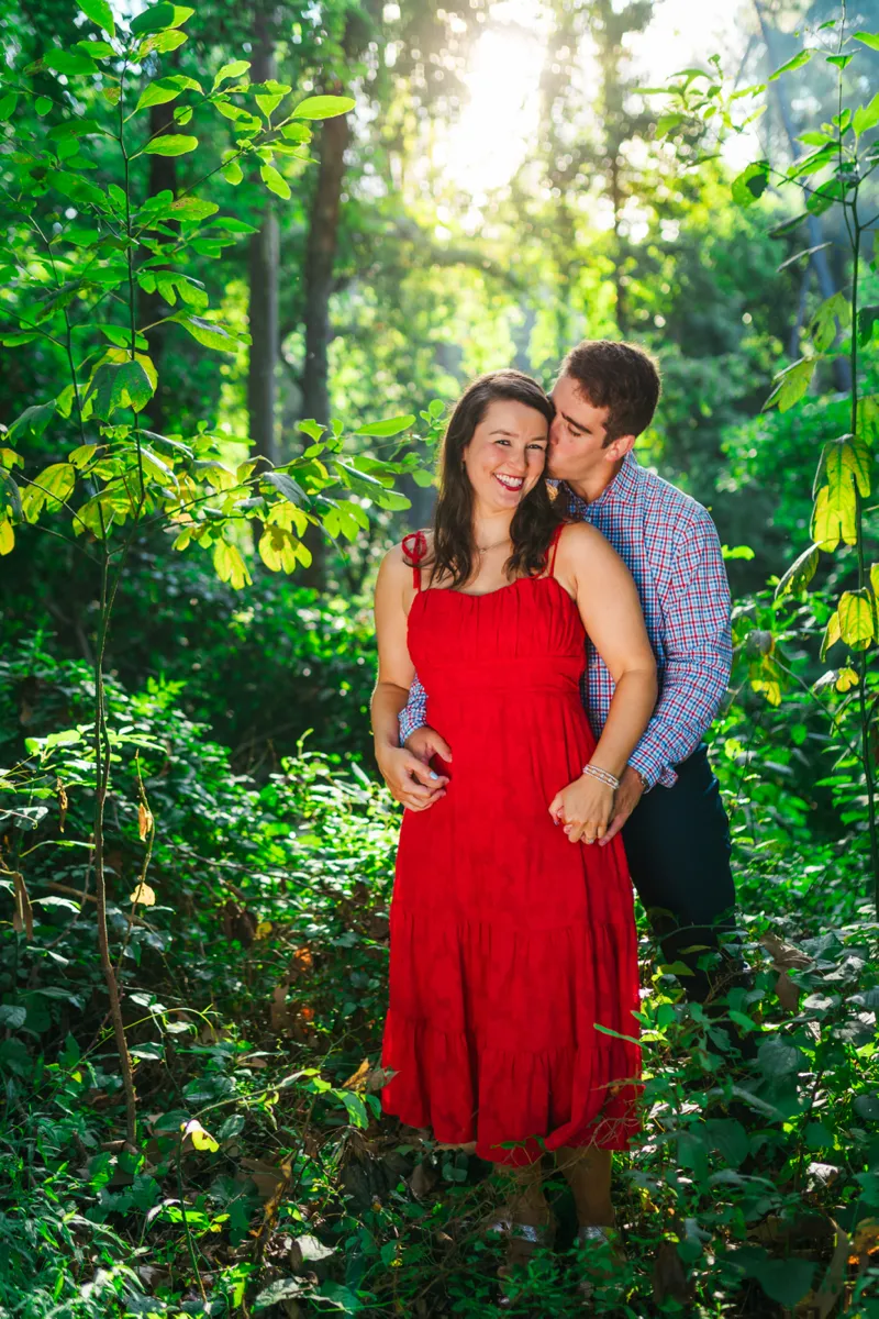 A couple laughing together in dense green woodland, sun breaking through the leaves