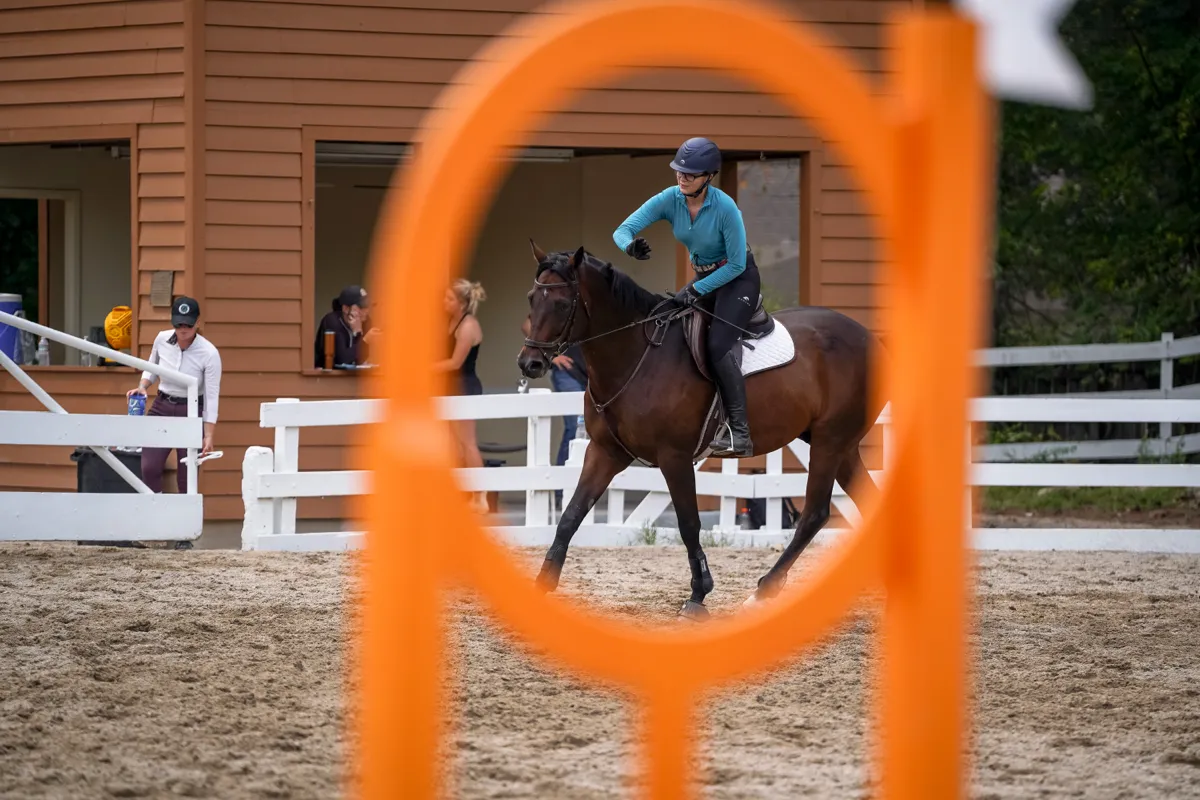 A horse and rider framed through the ring of an orange jump standard