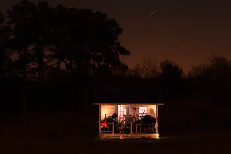 A small lit porch glowing warm against a deep blue night sky and dark trees