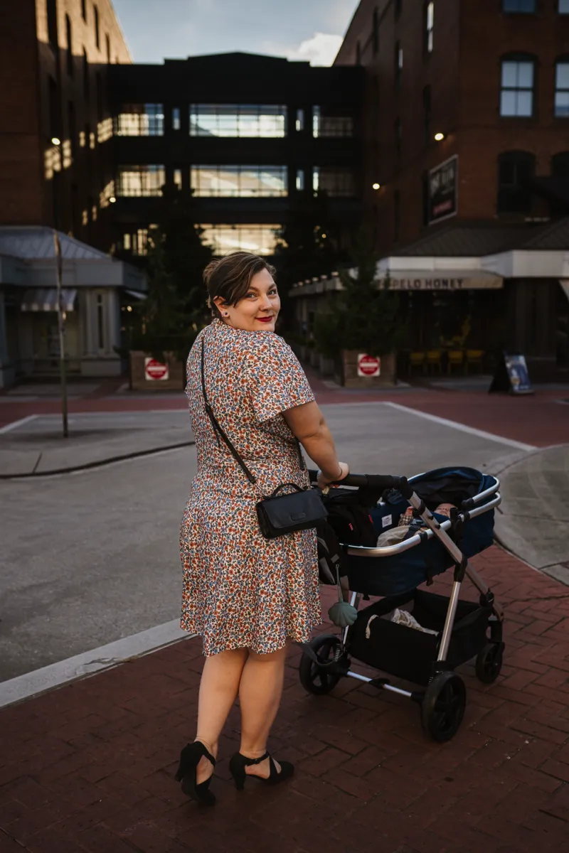 A mother glancing back over her shoulder while pushing a stroller through a city street at dusk