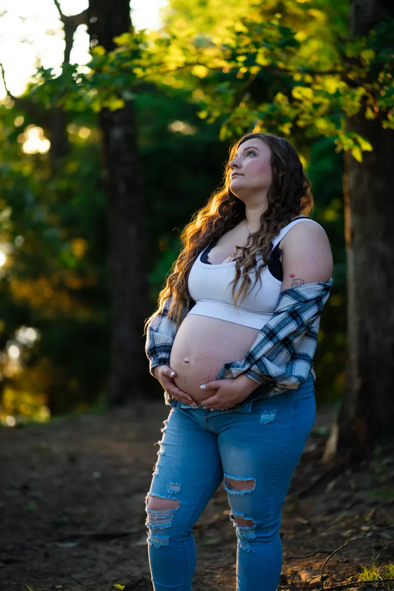 An expectant mother cradling her belly beneath sunlit trees