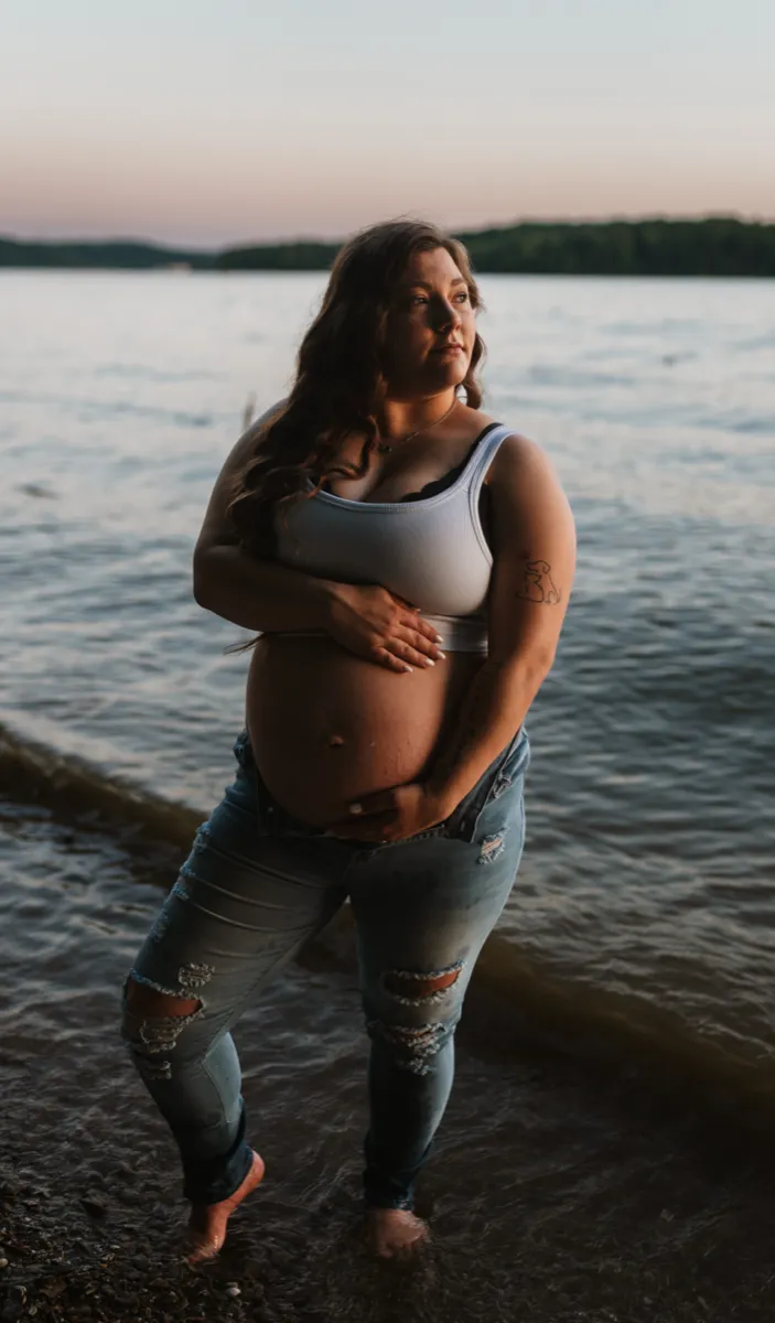 An expectant mother at the water's edge, both hands resting on her belly