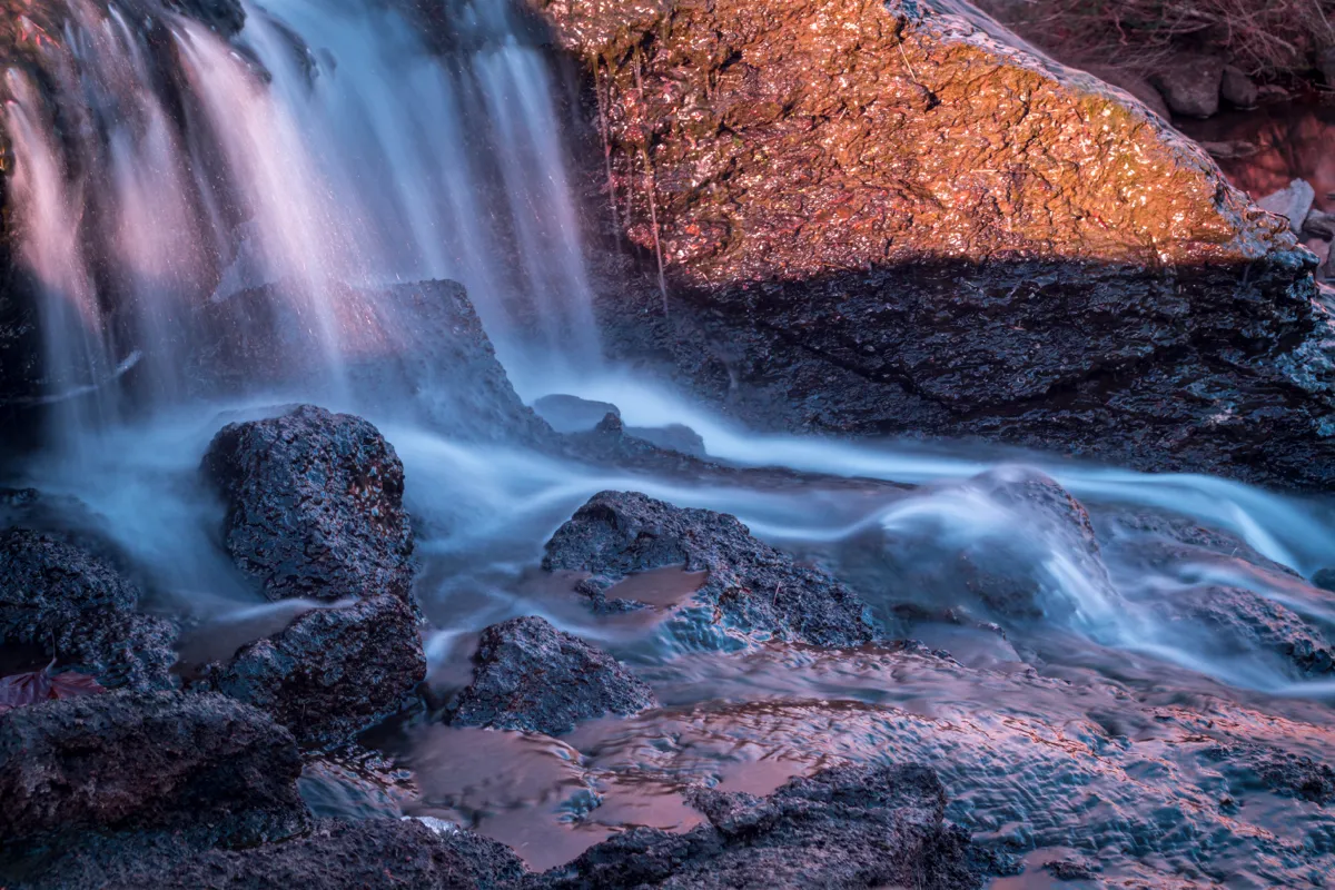 A waterfall spilling over dark rock, the water blurred smooth by a long exposure
