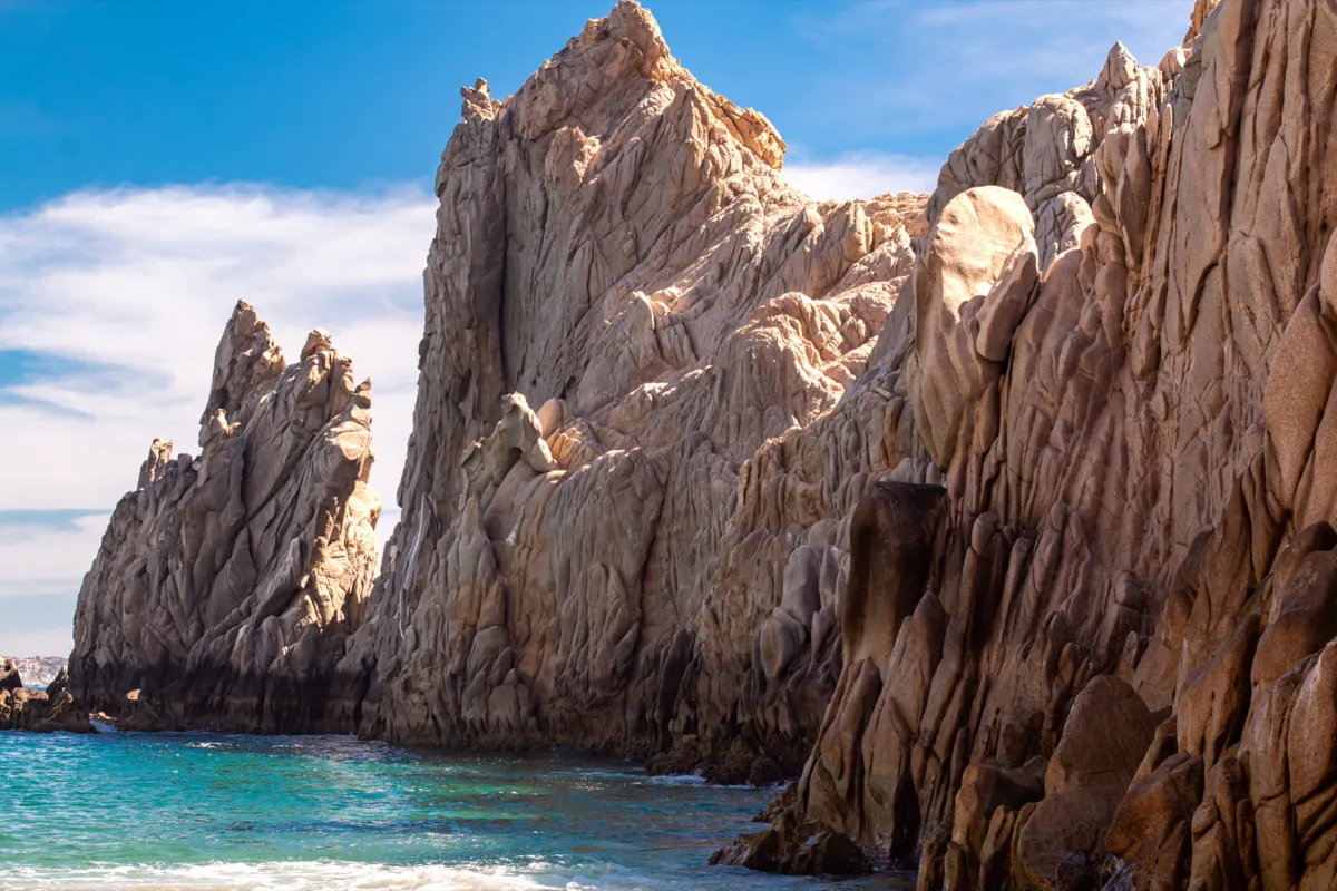 Sunlit rock formations rising from turquoise water along a rugged coast