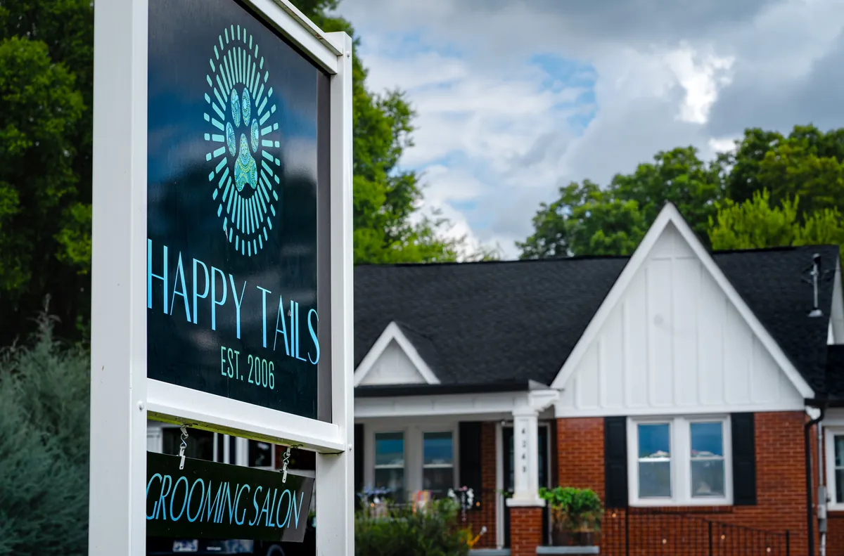 The Happy Tails sign, established 2006, standing in the grass in front of the salon's porch