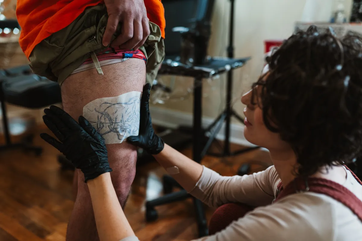 A tattoo artist at Velvet Ink Tattoo Studio in Fort Oglethorpe, Georgia, smoothing a purple stencil onto a client's thigh before starting