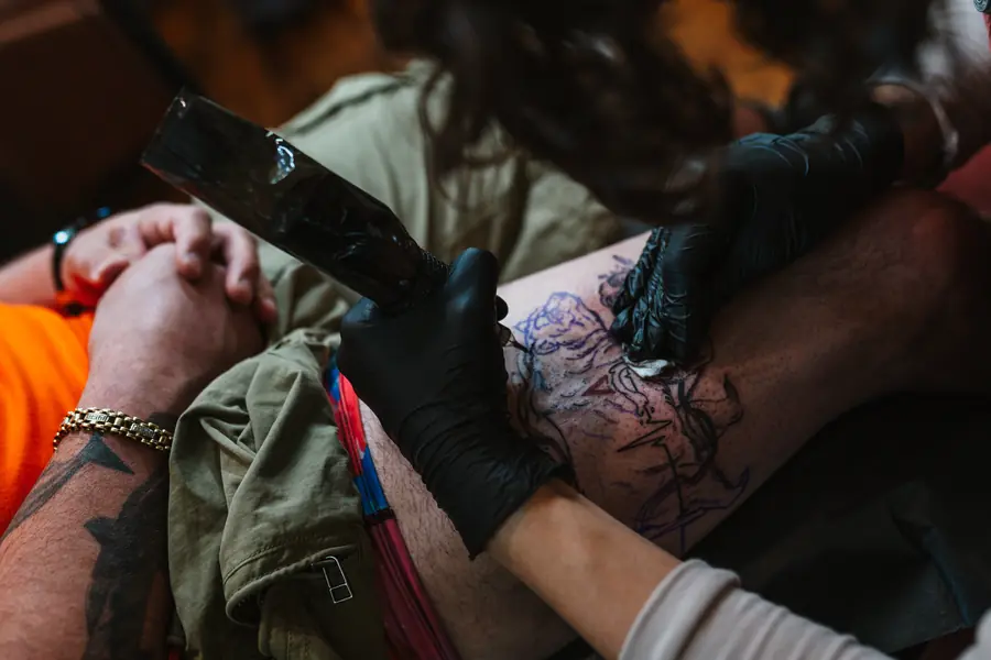 A tattoo artist's gloved hands inking over a purple stencil on a client's thigh at Velvet Ink Tattoo Studio in Fort Oglethorpe, Georgia
