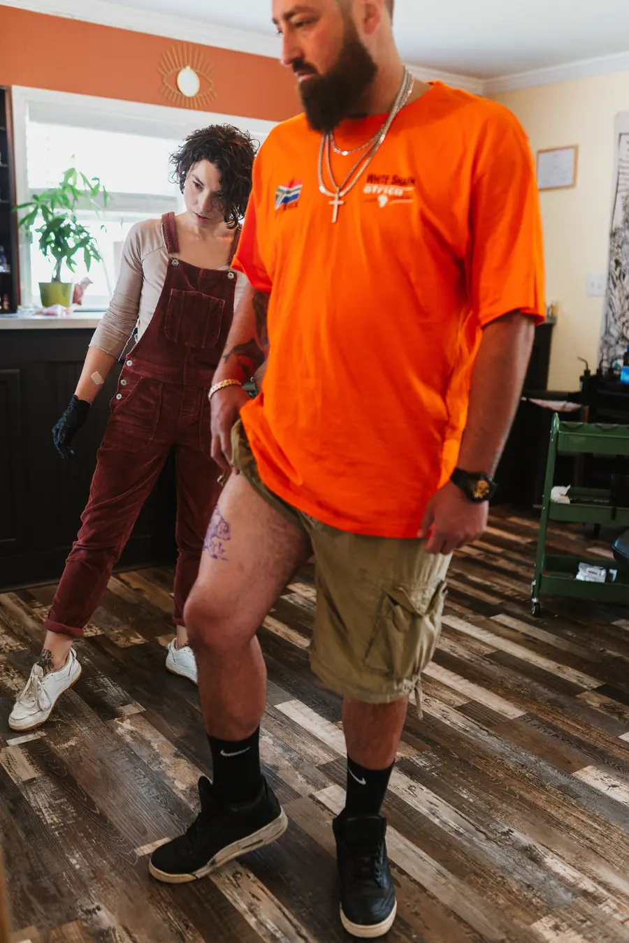 A tattoo artist at Velvet Ink Tattoo Studio in Fort Oglethorpe, Georgia, studying the stencil placement on a standing client's thigh before starting